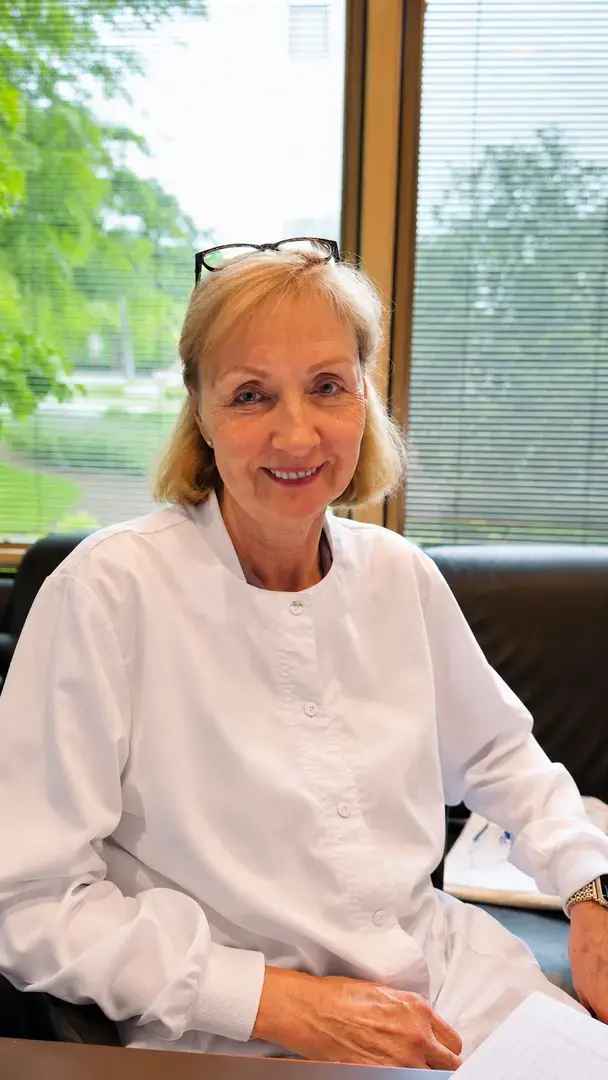 Smiling female doctor in a white coat seated in her office beside a window