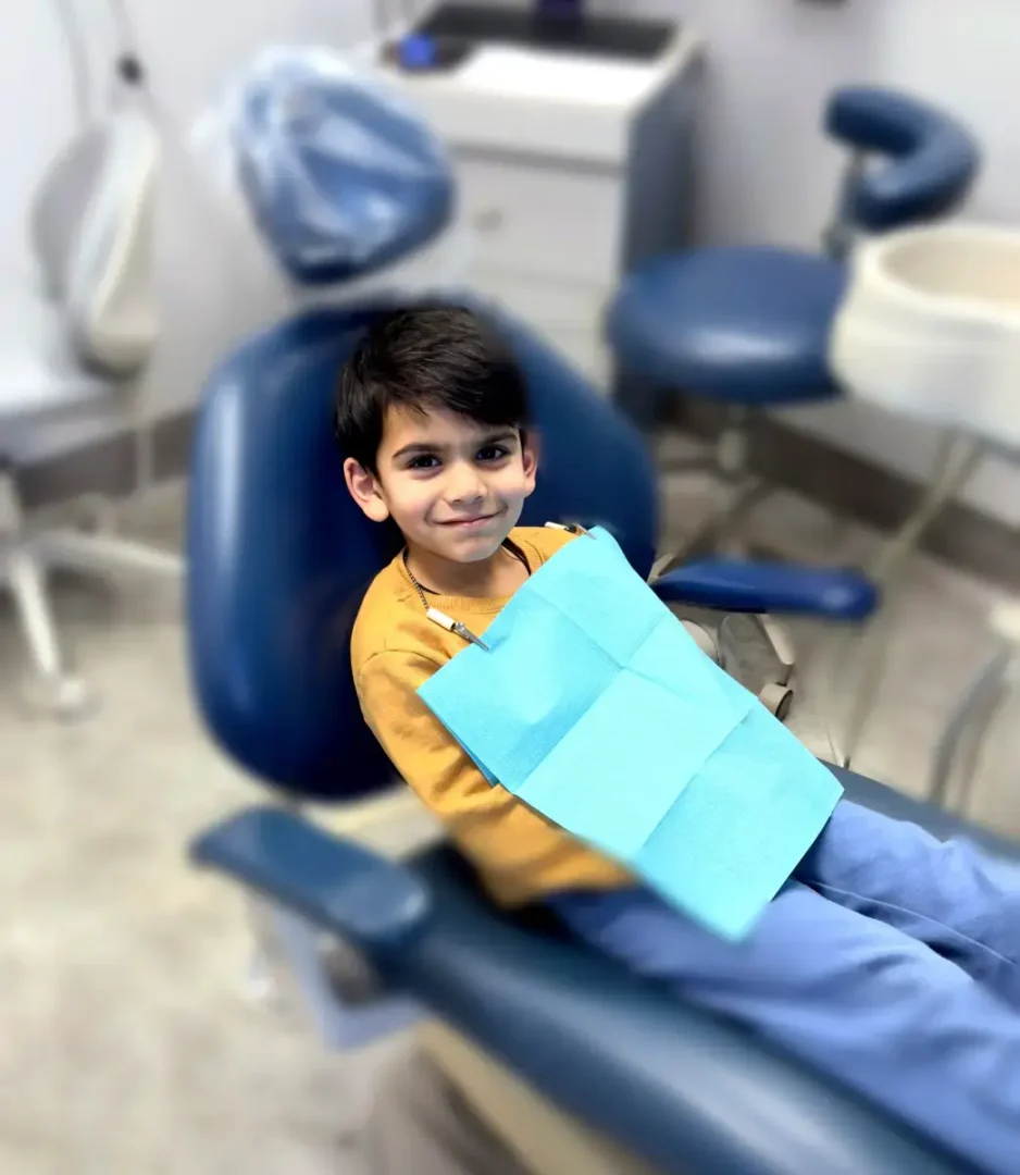 Young boy smiles in a dental chair wearing a blue bib at a Montville, NJ dental office
