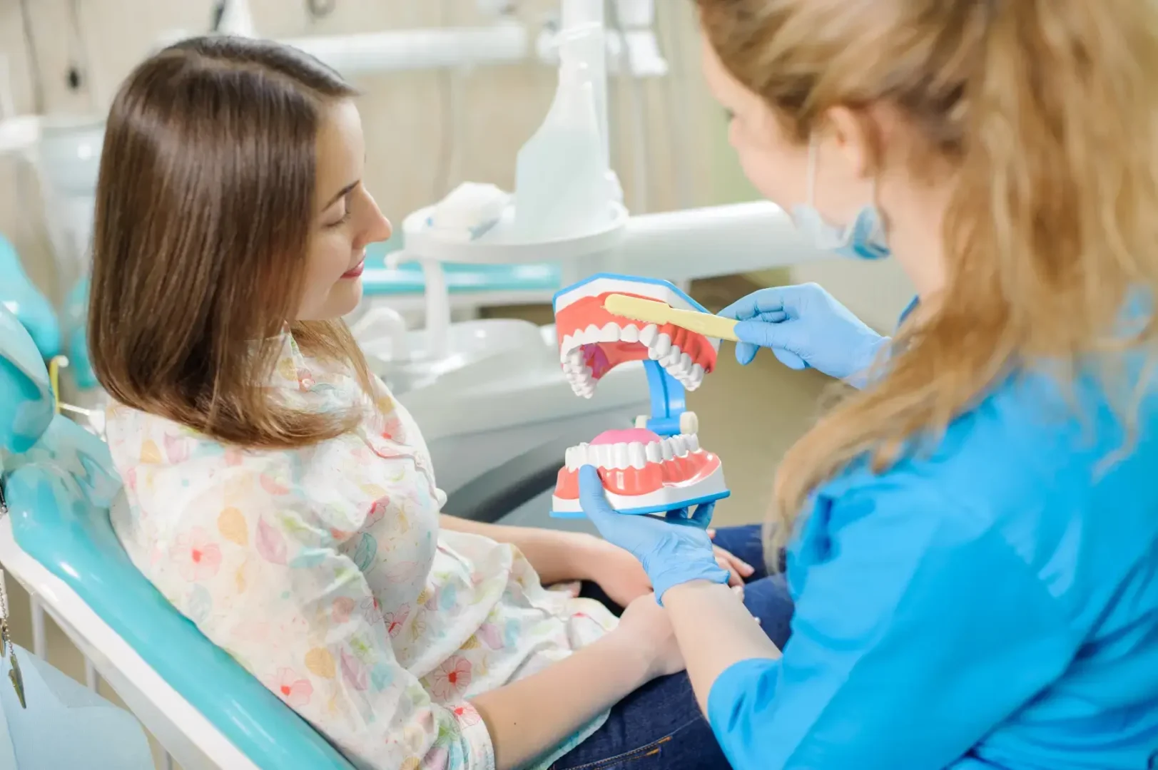 Dental professional shows a child how to brush using a model of teeth