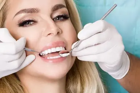 Dentist examines a woman's front teeth with a mirror during a porcelain veneers visit in Montville, NJ