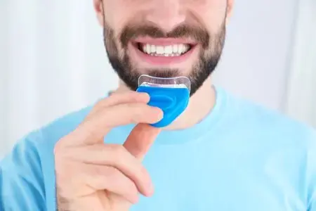 Teeth Whitening Home Kits in Montville, NJ for a Brighter Smile at Home Smiling man holds a custom teeth whitening tray near his mouth for at-home whitening in Montville, NJ