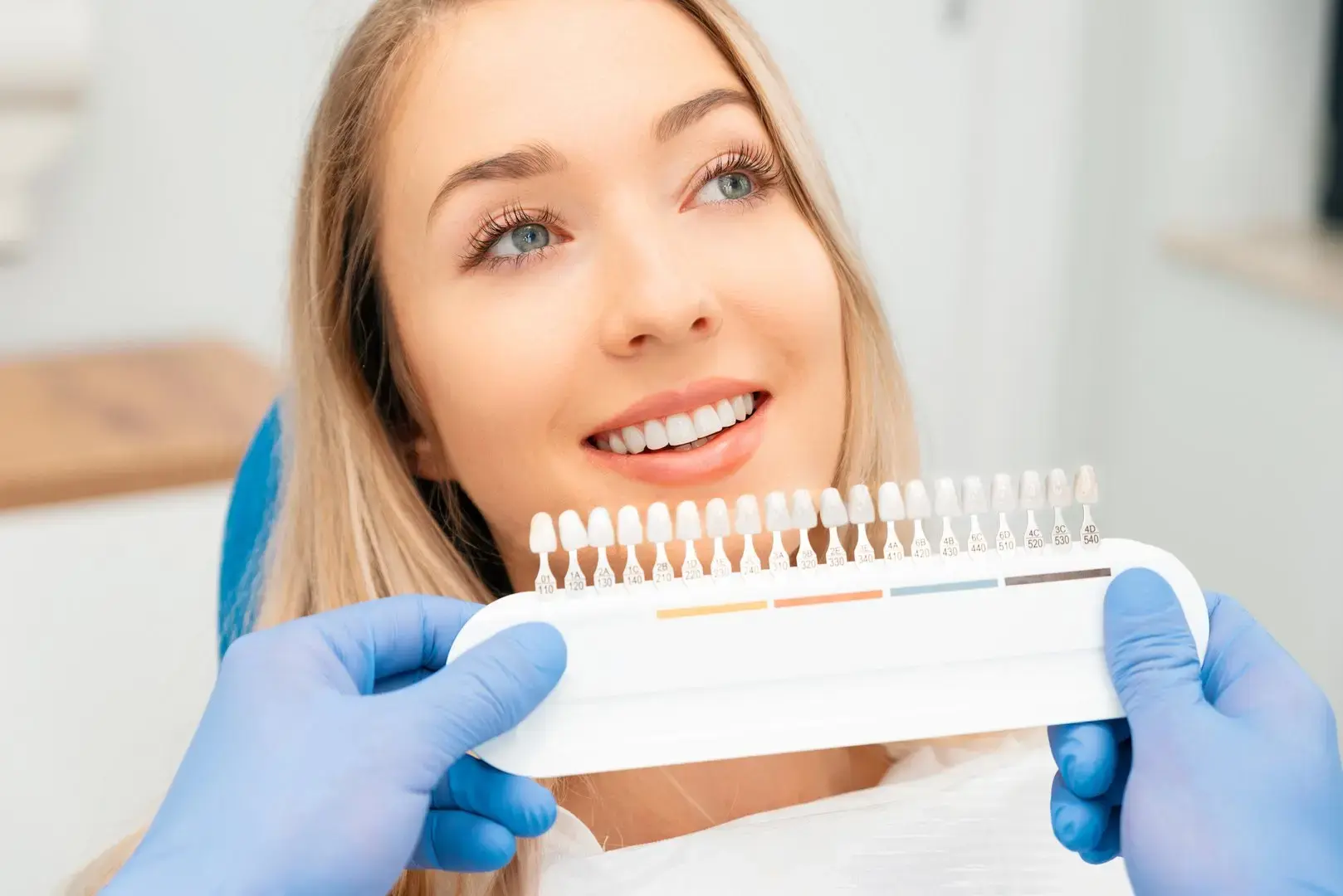 Dental professional compares a tooth shade guide with a patient's smile for cosmetic dentistry