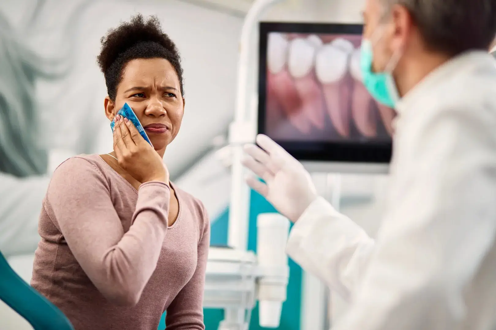 Woman holds an ice pack to her aching cheek while speaking with a dentist at an emergency dental visit in Montville, NJ